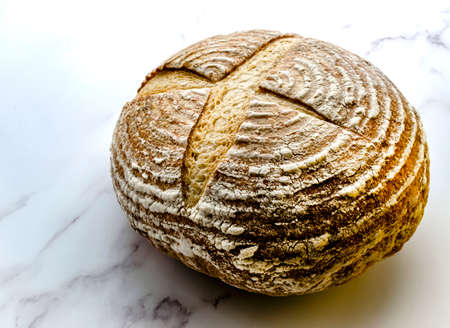 Freshly baked sourdough bread showing the traditional markings standing on a marble base