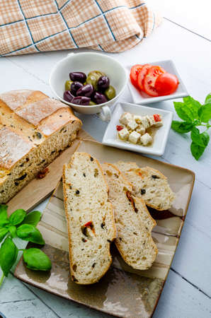 A view of three slices of olive bread together with feta cheese and tomatoes with the olive loaf and...