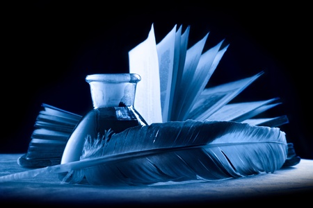 A feather with the bottle full of ink and a book in blueの写真素材