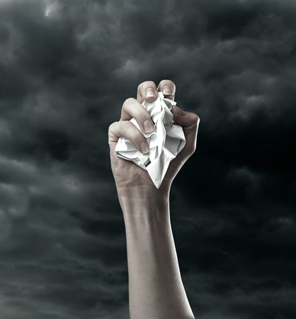Sheet of paper pressed in fist against stormy skyの写真素材