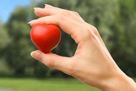 Female hand with red heart carefully holdingの写真素材