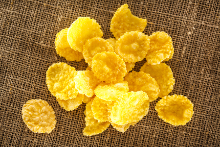 Wooden spoon and corn flakes on sack background closeup