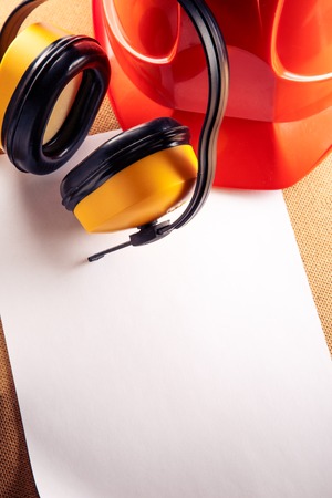 Red helmet, yellow earphones and blank sheet of paperの写真素材