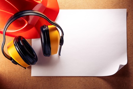 Red helmet, yellow earphones and blank sheet of paperの写真素材