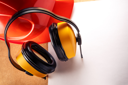 Red helmet, yellow earphones and blank sheet of paperの写真素材