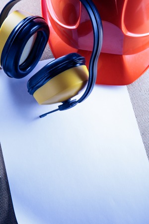 Red helmet, yellow earphones and blank sheet of paperの写真素材