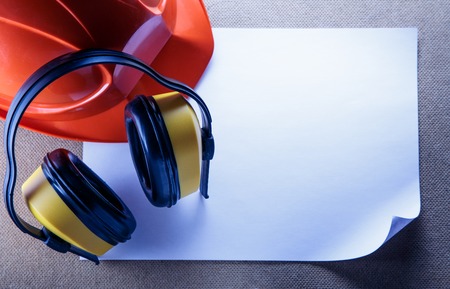 Red helmet, yellow earphones and blank sheet of paperの写真素材