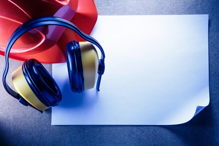 Red helmet, yellow earphones and blank sheet of paperの写真素材