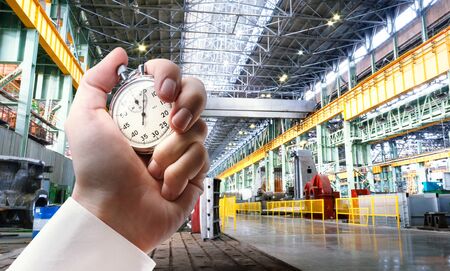 Machine shop of metallurgical works and stopwatch in male hand