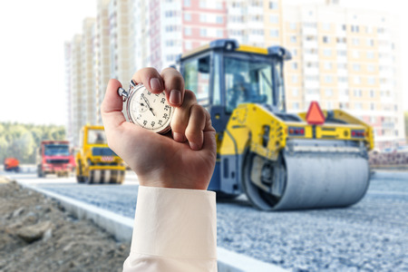 Road roller working and stopwatch in male handの写真素材