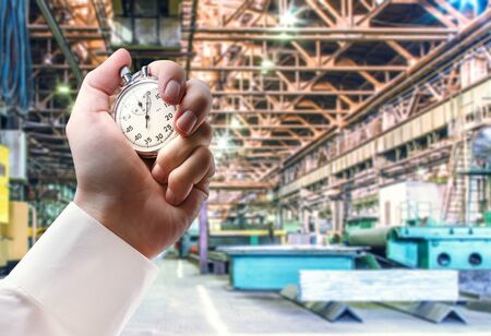 Machine shop of metallurgical works and stopwatch in male handの写真素材