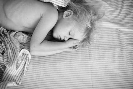 A child sleeps on a bed laying down hands at a head. Monochrome photo with place for textの写真素材