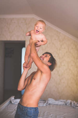 Young father playing with young son in bedroom. Pastel colours. The effect of film photographyの写真素材