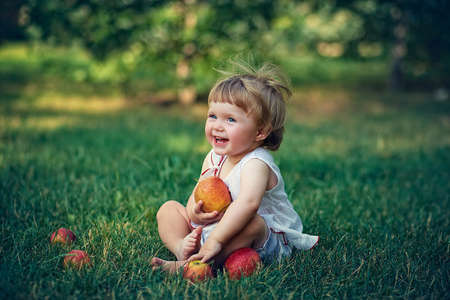 Little girl sitting on a green meadow with big apples in his hands. Positive facial expressionの写真素材