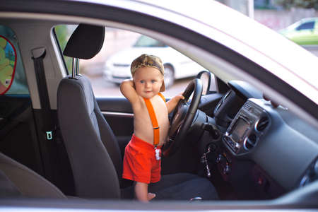 Little boy costs on front sitting of the car and holds a wheelの写真素材