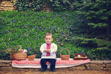 little boy in an embroidered shirt, sitting near the baskets with Easter cakesの写真素材