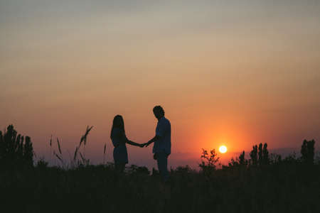 Couple in a field holding hands on sunset backgroundの写真素材