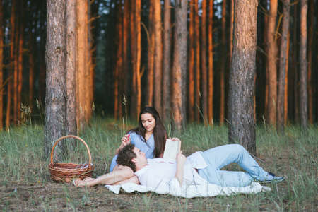 Man lies on a lap at the girl and reads the book in the woodの写真素材