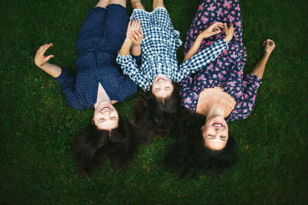 Mother and two young girls lying on a green lawn and smiling. The view from the top.の写真素材