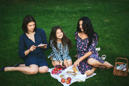 Beautiful family at the summer picnic. Mother and two young daughters relax on the lawn