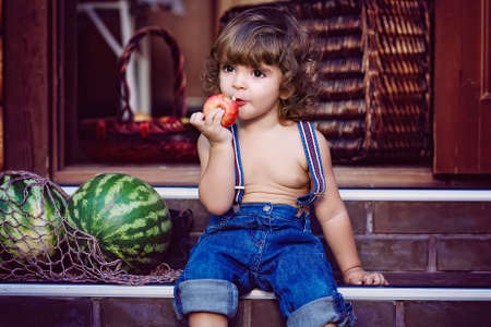 Little handsome boy sitting on the doorstep and eating an appleの写真素材