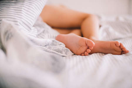 Cute little baby feet sticking out from under the blanket. The effect of film photographyの写真素材