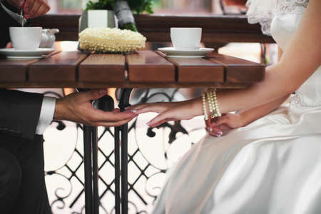 Gentle touch of the hands of the bride and groom under a table, on a table cups stand with coffeeの写真素材