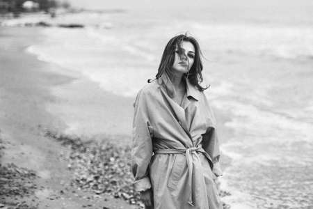 Girl ashore sea in an overcoat with the hair dishevelled by wind. The effect of film black and white photographyの写真素材