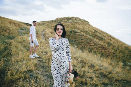 Pregnant woman in polka dot dress standing in wheat field and touching her hair and her manの写真素材