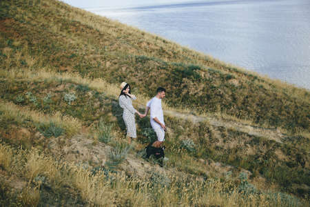 Outdoor portrait of walking young pregnant couple in field with dogの写真素材