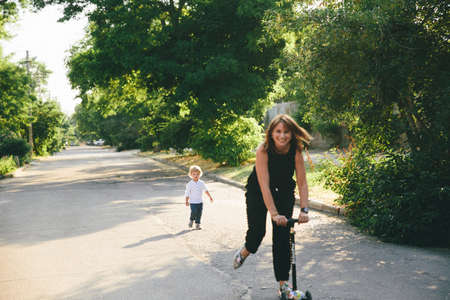 young mother is riding a scooter and a little son behind her.の写真素材