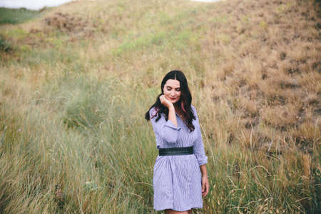 Smiling woman in a blue dress standing outdoors in a wheat field backgrond