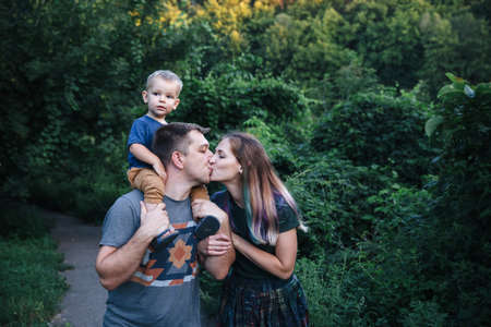 Happy young family father, mother and little son hugging and kissing outdoors, playing together in summer parkの写真素材