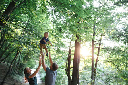 Happy joyful young family father, mother and little son having fun outdoors, playing together in summer parkの写真素材