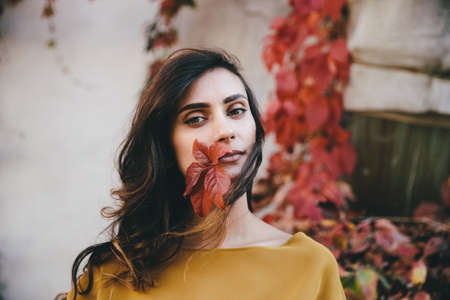 Young woman on autumn street with colorful leaves around. Orange leaves have fallen and are...