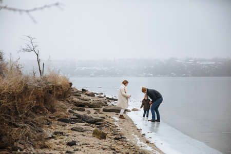 family in coats walking on the banks of a frozen riverの写真素材