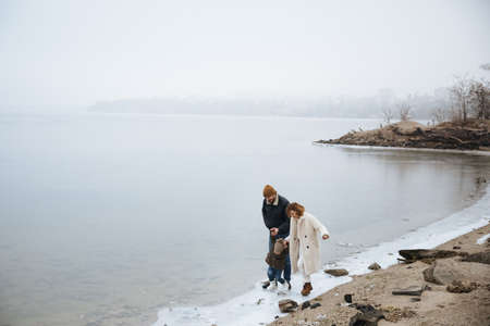 family in coats walking on the banks of a frozen riverの写真素材