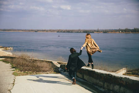 Young couple in warm coats having fun on the river bank.
