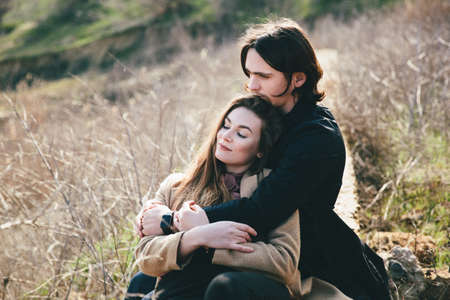 smiling couple sitting on countryside bulkhead against landscapeの写真素材