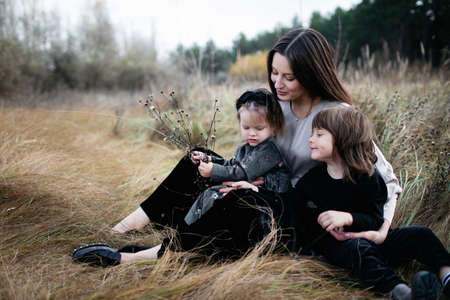 Close up portrait of woman with daughter and son on dry grass field. wheat field. family look. cute happy familyの写真素材