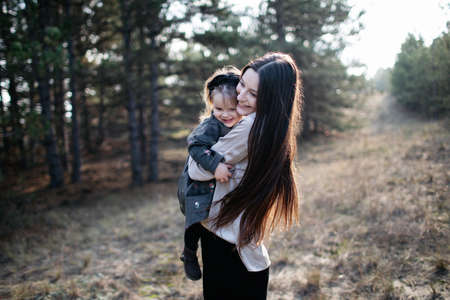 Young beautiful mom holds daughter in her arms and smiles on the forest background. Parenthood. Mom hugs daughterの写真素材