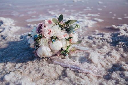 Beautiful bridal bouquet of white roses, peonies and eucalyptus and lace on the sea beach.の写真素材