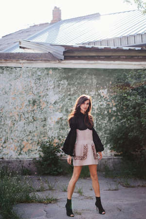Pretty brunette Model in a designer dress posing at camera on spring day on the old wall backgroundの写真素材