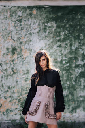 Pretty brunette Model in a designer dress posing at camera on spring day on the old wall backgroundの写真素材