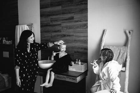 Mom and Two smiling kids brother and sister in unicorn bathrobes brush their teeth after having bath