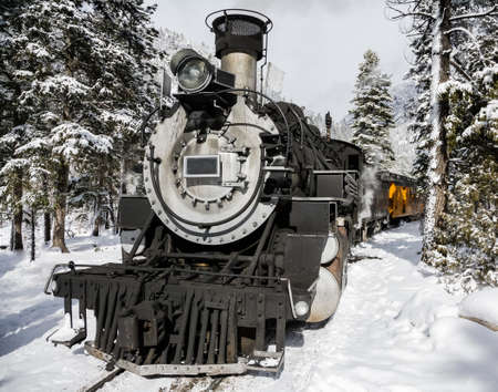 Vintage Railroad Steam Locomotive Pulling Passenger Cars in the Snow Filled Mountins.