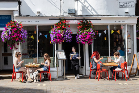 09/02/2019 Winchester, Hampshire, UK the front of a cafe with people sitting at tables in the sun enjoying food and a coffee with a waitress carrying a tray waiting on tablesのeditorial素材