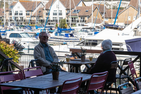 09/14/2019 Portsmouth, Hampshire, UK An elderly couple enjoying a drink outside in a restaurant at a yacht marinaのeditorial素材