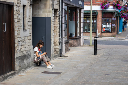 09/02/2019 Winchester, hampshire, UK An Asian lady in her twenties looking at her mobile phone whilst sat on a step outside a shop on a high streetのeditorial素材