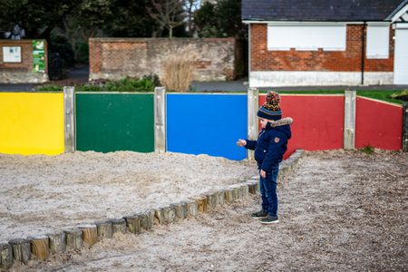 01/28/2020 Portsmouth, Hampshire, UK a child standing alone in a park next to a sand pit with sand in his handのeditorial素材